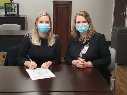 Two women wearing face masks sitting at desk in offfice